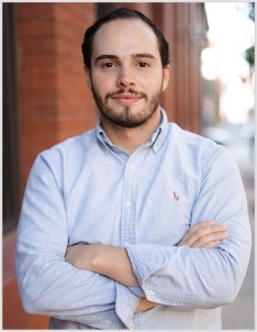 A person wearing a shirt and tie standing in front of a brick wall.