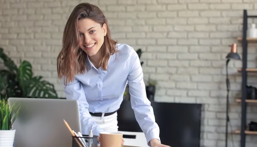 Woman standing over desk and looking at a laptop. smiling.
