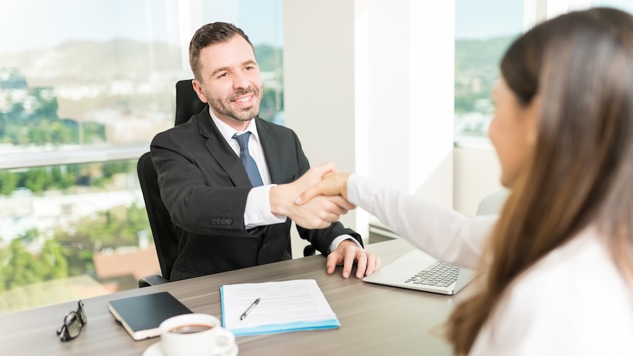 A person in a suit and tie is shaking hands with a person in a white shirt and red tie.