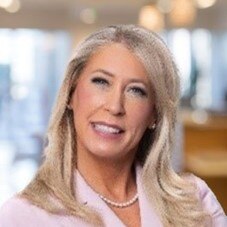 A person with long hair wearing a blue dress shirt and a pink tie.