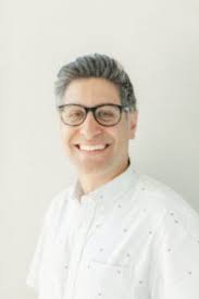 A person wearing glasses and a bow tie smiles.