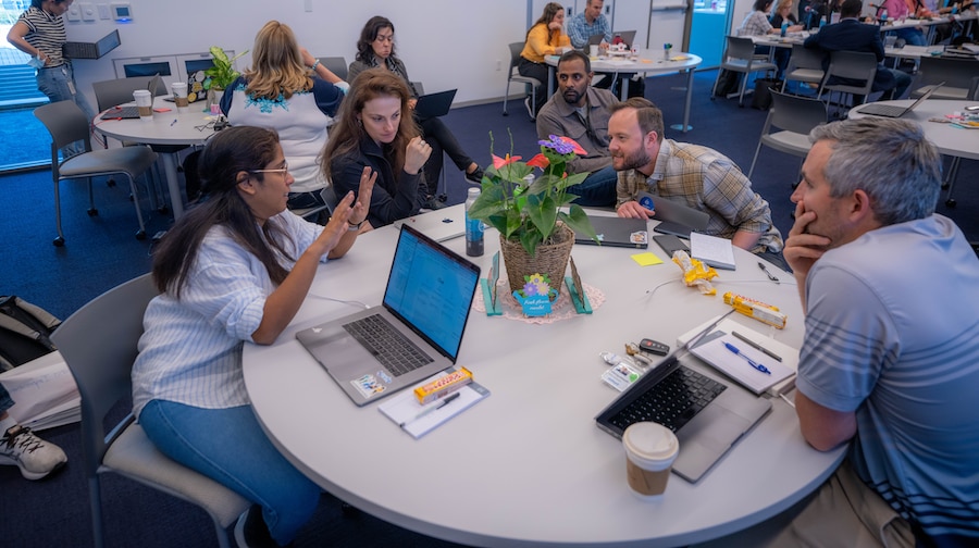 A group of people sitting around a table with laptops.