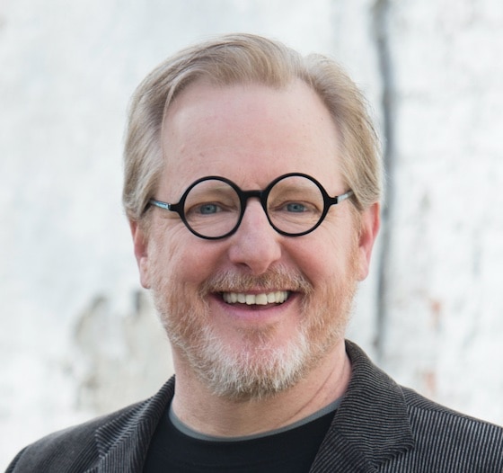 A person with glasses smiling and wearing a black shirt and glasses.