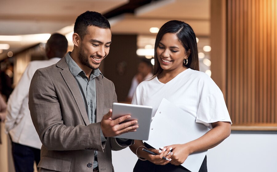 A businessman and businesswoman smiling and discussing strategy on their device.