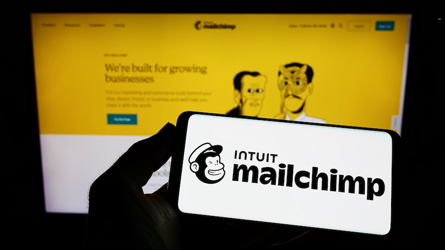 A person holding the Intuit Mailchimp app on their phone, and looking at the Intuit Mailchimp website on their laptop.