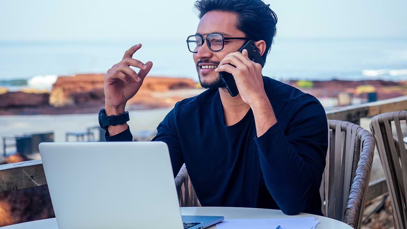 A person sitting at a table with a laptop and cell phone.