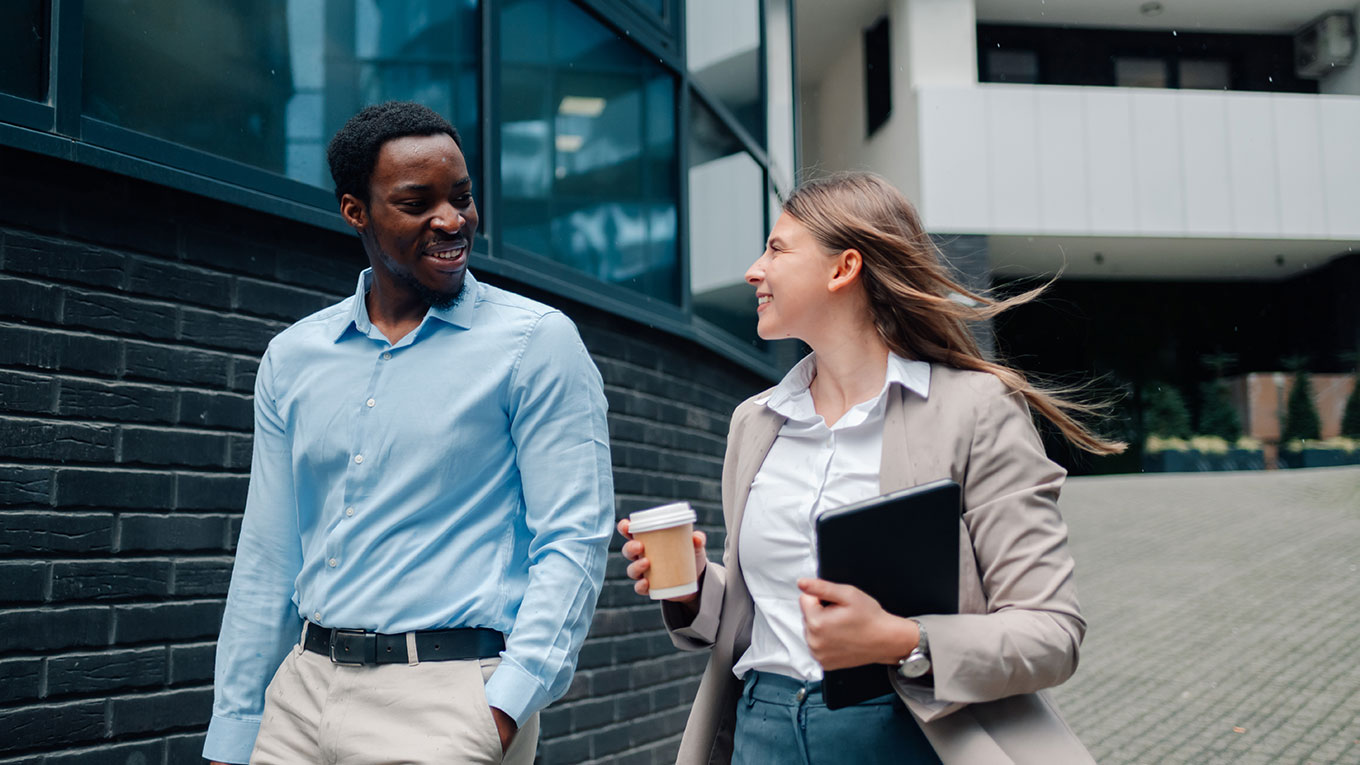 Two accounting colleagues walk in front of an office building discussing QuickBooks.