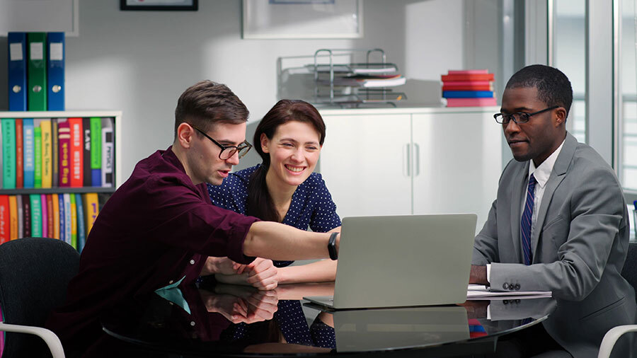 A group of people sitting around a laptop computer.