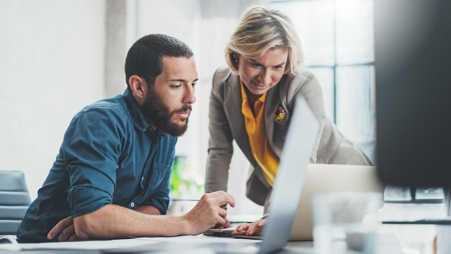 Two businesspeople looking at QuickBooks Online Payroll on a laptop.