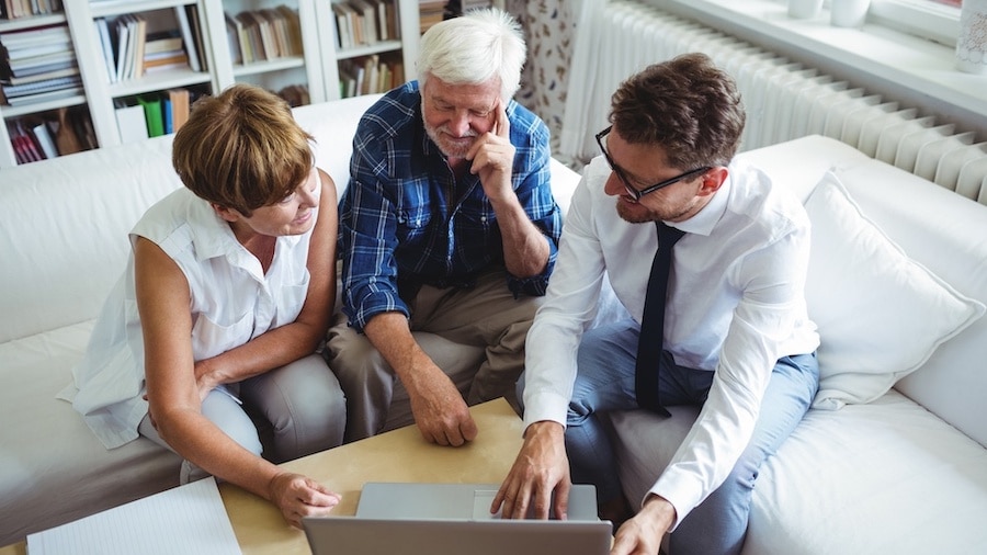 Three people sitting on a couch looking at a laptop.