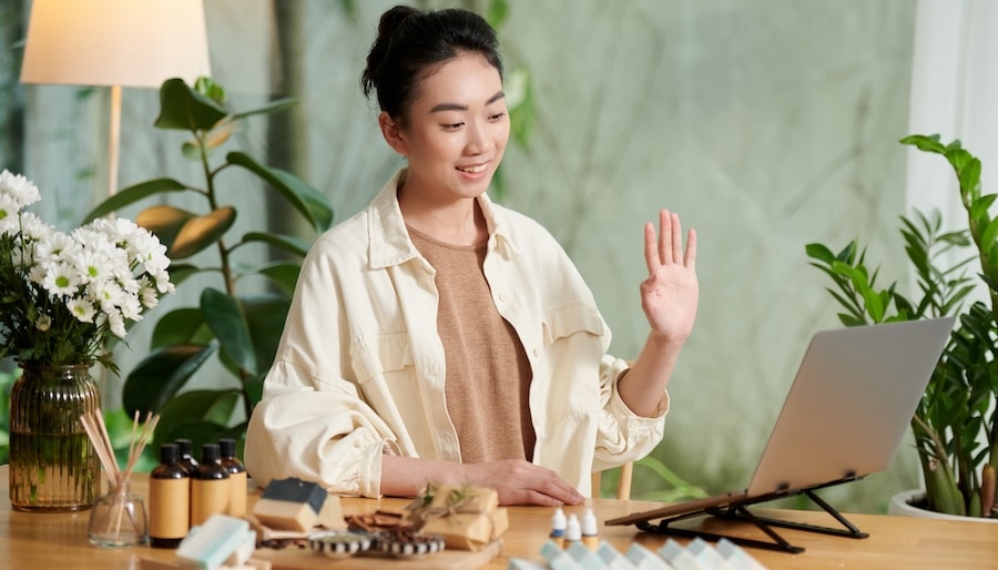 A woman smiling and holding her hand up while on a video call.
