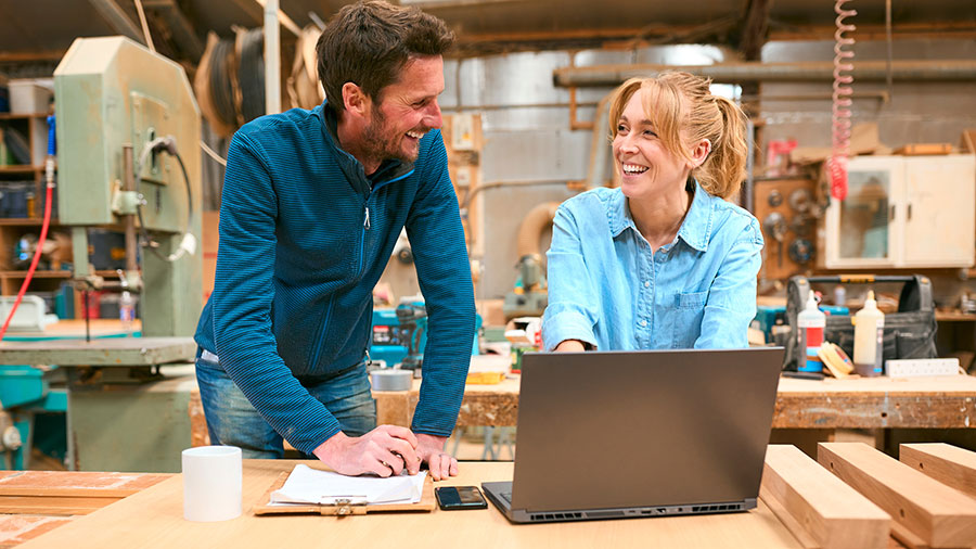 Two people are smiling while sitting at a laptop.
