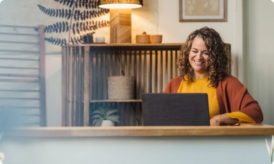 A business owner smiling and sitting at a desk with a laptop.